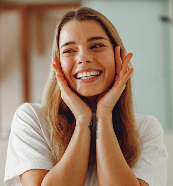 Smiling woman with hands to face in bright dental office setting, displaying healthy teeth and happiness.