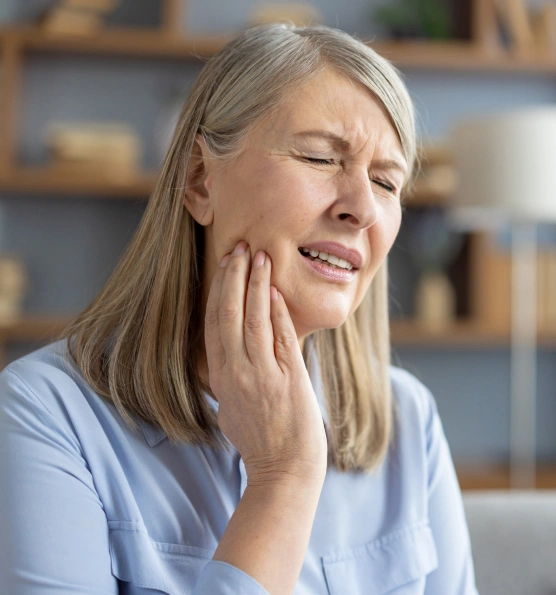 Woman with hand to cheek experiencing tooth pain or discomfort indoors