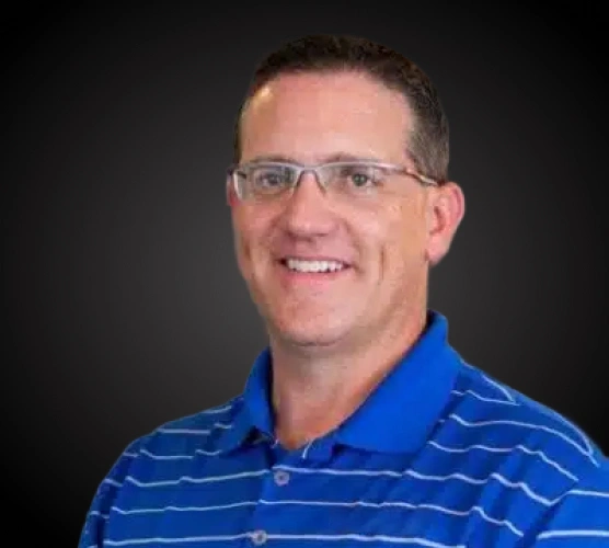 Professional headshot of male dentist wearing blue striped polo shirt and glasses against dark background.