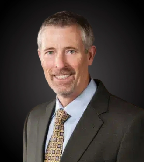 Professional headshot of male dentist in business suit against dark background