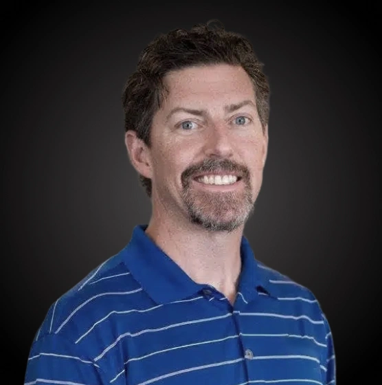 Professional headshot of male dentist in blue striped polo shirt against dark background.
