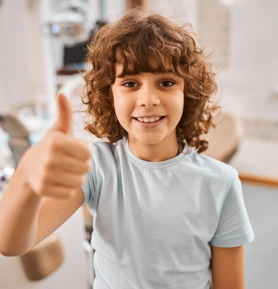 Happy child giving thumbs up in dental office wearing light blue shirt
