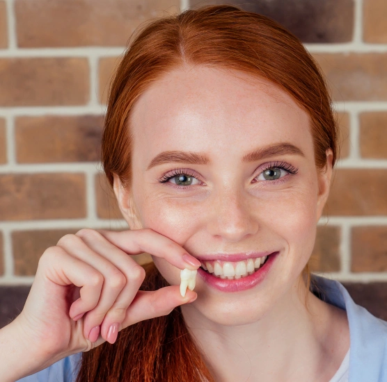 Smiling young woman with red hair against brick wall background for dental practice.