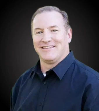 Professional headshot of male dentist in navy blue shirt against dark background.