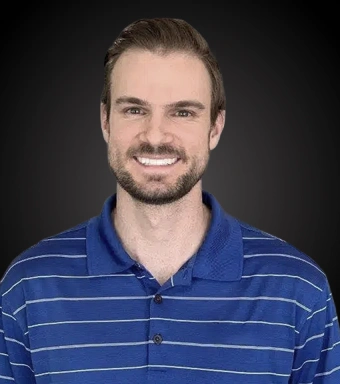 Professional headshot of smiling male staff member wearing blue striped polo shirt against dark background.