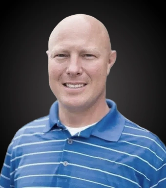 Professional headshot of male dentist wearing blue striped polo shirt against dark background.
