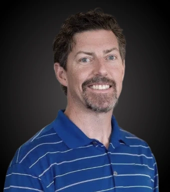 Professional headshot of male dentist wearing blue striped polo shirt against dark background.