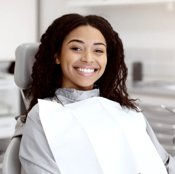Smiling female patient wearing dental bib in modern dental office chair