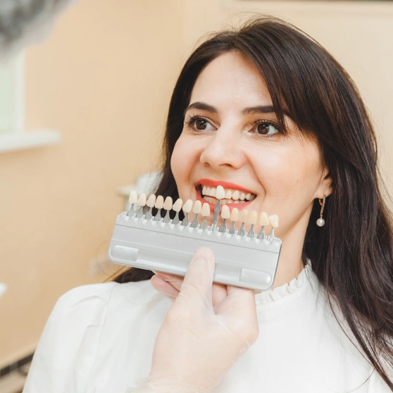Woman holding dental shade guide in dental office, smiling at camera.