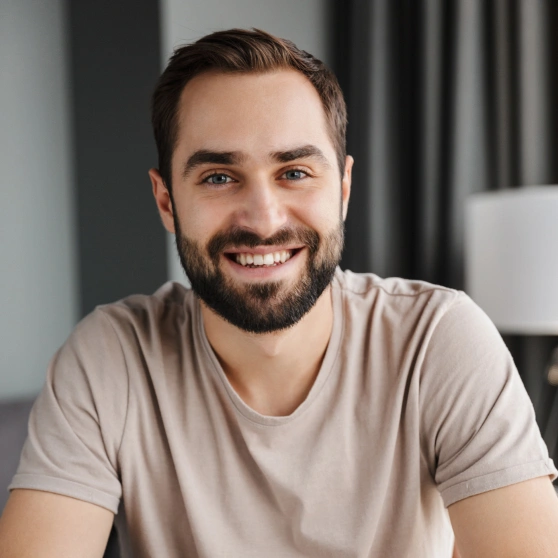 Smiling male dental professional in casual beige shirt, modern office setting with white shelving background.