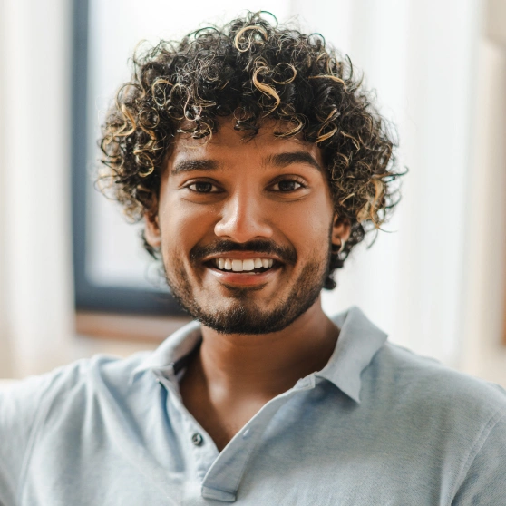 Smiling man with curly hair in light blue shirt, professional headshot in modern office setting.