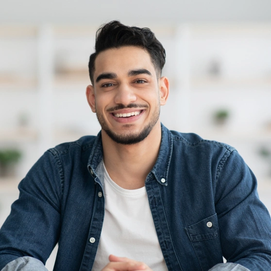 Smiling young man in denim shirt against blurred office background at dental practice.