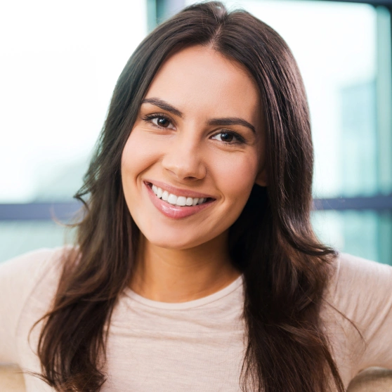 Professional headshot of smiling woman in modern dental office setting with glass windows