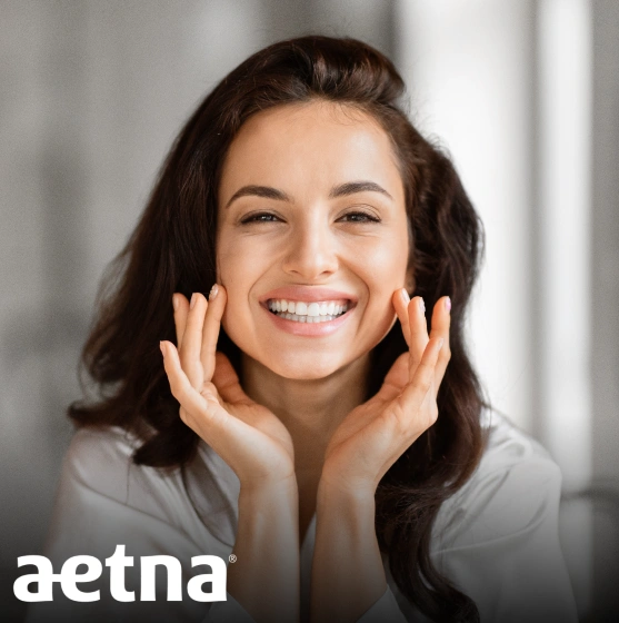 Smiling woman with hands on face in dental office, Aetna logo visible.