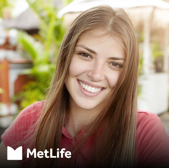 Young woman smiling at camera indoors with plants and MetLife logo visible behind her.